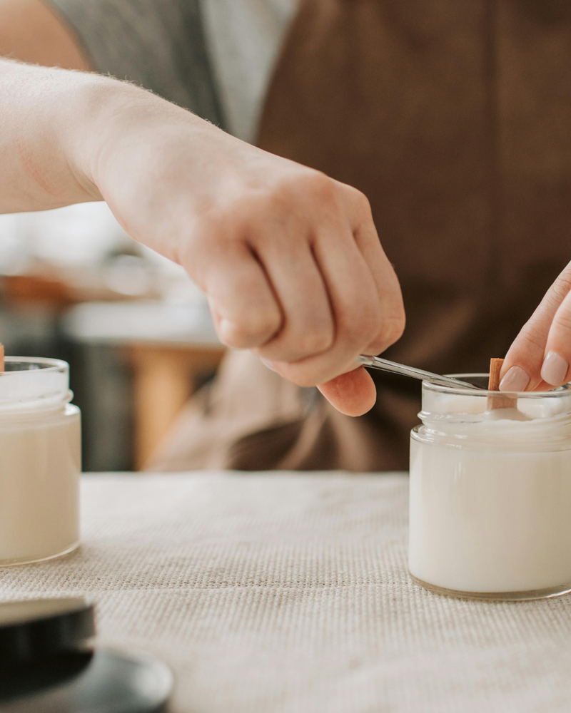 Person using a spoon to scoop something from a jar on a table.